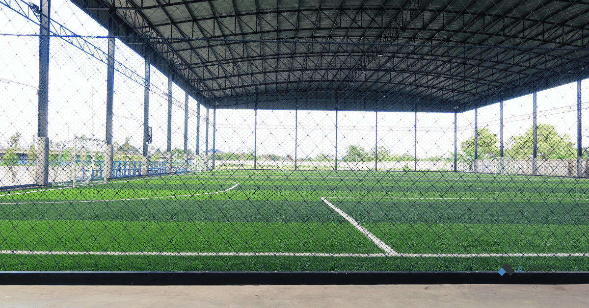 Indoor sports complex featuring green rubber backed turf athletic facilities enclosed by protective netting.